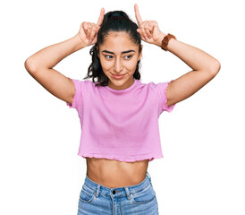 Wall Mural - Hispanic teenager girl with dental braces wearing casual clothes doing funny gesture with finger over head as bull horns