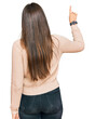 © Krakenimages.com - Young brunette woman wearing casual winter sweater posing backwards pointing ahead with finger hand