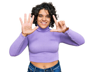 Canvas Print - Young hispanic woman with curly hair wearing casual clothes showing and pointing up with fingers number seven while smiling confident and happy.