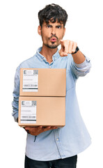 Sticker - Young hispanic man holding delivery package pointing with finger to the camera and to you, confident gesture looking serious