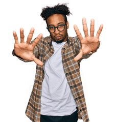 Wall Mural - Young african american man with beard wearing casual clothes and glasses doing frame using hands palms and fingers, camera perspective