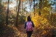 © KumCup - Person with pink backpack hiking in a sunlit autumn forest with colorful leaves.