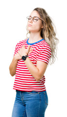 Wall Mural - Beautiful young blonde woman wearing glasses over isolated background smiling with hands on chest with closed eyes and grateful gesture on face. Health concept.