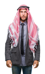 Young handsome arabian man with long hair wearing keffiyeh over isolated background with serious expression on face. Simple and natural looking at the camera.