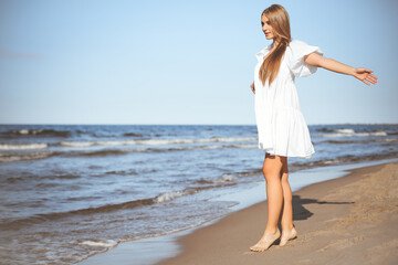 Happy smiling beautiful woman is walking on the ocean beach with open arms