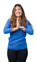 Young beautiful brunette woman wearing blue sweater over isolated background begging and praying with hands together with hope expression on face very emotional and worried. Asking for forgiveness