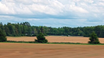 Wall Mural - Car view of harvested agricultural fields with forests in the distance, an autobahn on the other side, under cloudy sky. Sweden.