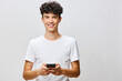 © SHOTPRIME STUDIO - smiling young man with smartphone standing against light background, modern lifestyle concept, casual attire, technology and connection theme, happy expression, youth engagement, innovation