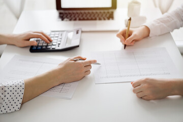 Accountant using a calculator and laptop computer for counting taxes with a client or a colleague at white desk in office. Teamwork in business audit and finance