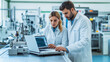 © Катерина Євтехова - Collaboration between a male and female engineer on the factory floor, with advanced machinery in the background, they are focused on the data displayed on a laptop, emphasizing th