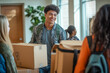 © ZaStock - A young man with curly hair carries moving boxes, smiling at his friends in a well-lit room filled with people and greenery
