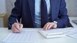 © volha_r - Businessman accountant with blue suit is using white calculator and taking notes with a silver pen. Taxes and audit concept