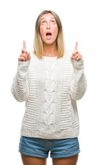 Young beautiful woman wearing winter sweater over isolated background amazed and surprised looking up and pointing with fingers and raised arms.