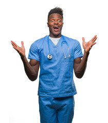 Canvas Print - Young african american doctor man over isolated background wearing surgeon uniform celebrating crazy and amazed for success with arms raised and open eyes screaming excited. Winner concept