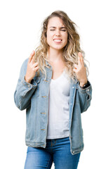 Wall Mural - Beautiful young blonde woman wearing denim jacket over isolated background smiling crossing fingers with hope and eyes closed. Luck and superstitious concept.