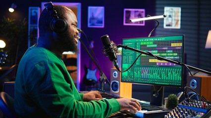 Aufkleber - Artist recording new tracks by playing piano notes on electronic keyboard in his home studio, working with audio stereo gear to mix and master tunes. African american musician. Camera B.