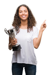 Sticker - Young hispanic woman holding trophy very happy pointing with hand and finger to the side