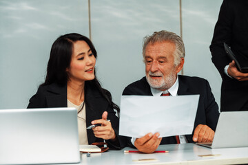 Wall Mural - Senior caucasian manager working in office with assistance of young Asian business people and translator in meeting. Corporate international business and secretary language translation concept. uds