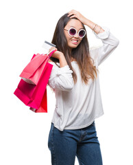 Sticker - Young asian woman holding shopping bags on sales over isolated background stressed with hand on head, shocked with shame and surprise face, angry and frustrated. Fear and upset for mistake.