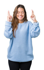 Wall Mural - Young beautiful brunette woman wearing blue winter sweater over isolated background smiling crossing fingers with hope and eyes closed. Luck and superstitious concept.