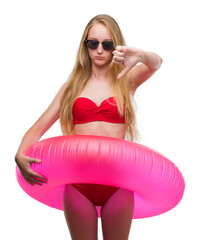 Poster - Blonde teenager woman wearing bikini and holding pink floater with angry face, negative sign showing dislike with thumbs down, rejection concept