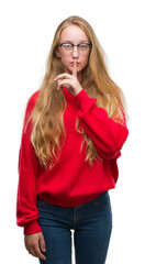 Sticker - Blonde teenager woman wearing red sweater asking to be quiet with finger on lips. Silence and secret concept.