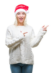 Canvas Print - Young beautiful blonde woman wearing christmas hat over isolated background smiling and looking at the camera pointing with two hands and fingers to the side.