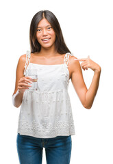 Wall Mural - Young asian woman drinking glass of water over isolated background with surprise face pointing finger to himself