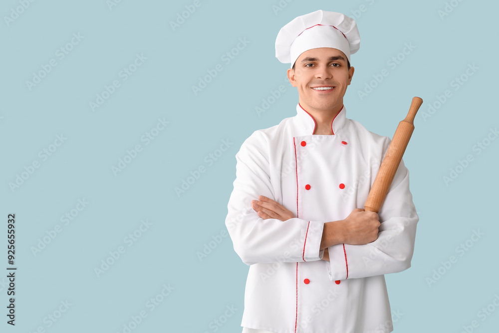 Handsome happy male chef with rolling pin on blue background