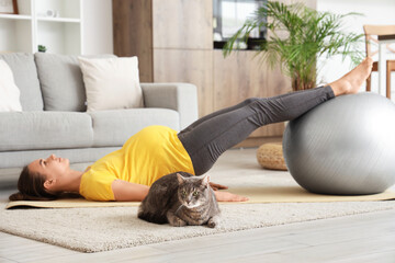 Wall Mural - Young pregnant woman with fitball and cat practicing yoga at home