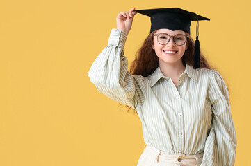 Wall Mural - Happy female student in graduation hat on yellow background