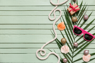 Wall Mural - Sunglasses, Christmas balls with  shells on palm branch, rope and gift box on green wooden background. Top view