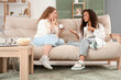 © Pixel-Shot - Young women having cup of tea on sofa in living room