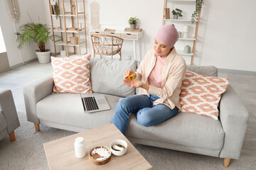 Wall Mural - Mature woman after chemotherapy taking weed from bottle on sofa at home