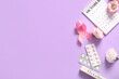 © Pixel-Shot - Composition with pink ribbon, pills, calendar and flowers on lilac background. Breast cancer awareness concept