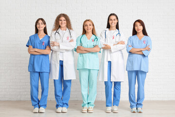 Poster - Female doctors with pink ribbons on white brick background. Breast cancer awareness concept