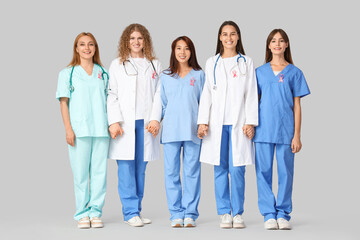 Poster - Female doctors with pink ribbons holding hands on light background. Breast cancer awareness concept