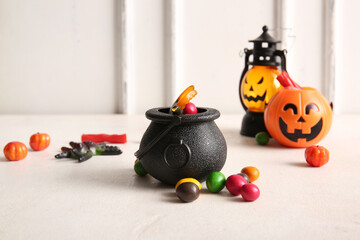 Pot with sweet treats and lanterns for Halloween on light table