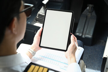 Over shoulder view of pilot wearing sunglasses using digital tablet in the cockpit of an airplane