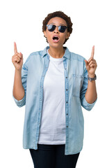 Sticker - Beautiful young african american woman wearing sunglasses over isolated background amazed and surprised looking up and pointing with fingers and raised arms.