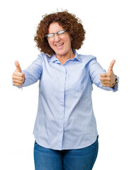 Wall Mural - Beautiful middle ager senior businees woman wearing glasses over isolated background approving doing positive gesture with hand, thumbs up smiling and happy for success. Looking at the camera