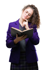 Wall Mural - Young brunette student girl wearing school uniform reading a book over isolated background serious face thinking about question, very confused idea