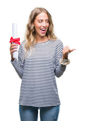 Wall Mural - Beautiful young blonde woman holding degree certificate over isolated background pointing and showing with thumb up to the side with happy face smiling