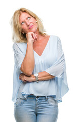 Wall Mural - Middle age blonde business woman over isolated background with hand on chin thinking about question, pensive expression. Smiling with thoughtful face. Doubt concept.