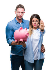 Wall Mural - Young couple in love holding piggy bank over isolated background with open hand doing stop sign with serious and confident expression, defense gesture