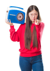 Canvas Print - Young Chinese woman over isolated background holding vintage radio pointing with finger to the camera and to you, hand sign, positive and confident gesture from the front