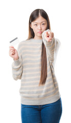 Canvas Print - Young Chinese woman over isolated background holding credit card pointing with finger to the camera and to you, hand sign, positive and confident gesture from the front