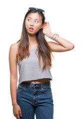 Poster - Young asian woman wearing sunglasses over isolated background smiling with hand over ear listening an hearing to rumor or gossip. Deafness concept.