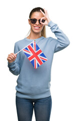 Poster - Beautiful young woman holding UK flag with happy face smiling doing ok sign with hand on eye looking through fingers