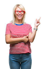 Canvas Print - Young beautiful blonde woman wearing glasses over isolated background with a big smile on face, pointing with hand and finger to the side looking at the camera.